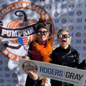 Two children posing against a Pumpkin Run backdrop with a RogersGray-branded photo prop